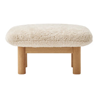 Cream faux sheepskin ottoman with natural wood legs, featuring a soft, textured surface and rounded shape.