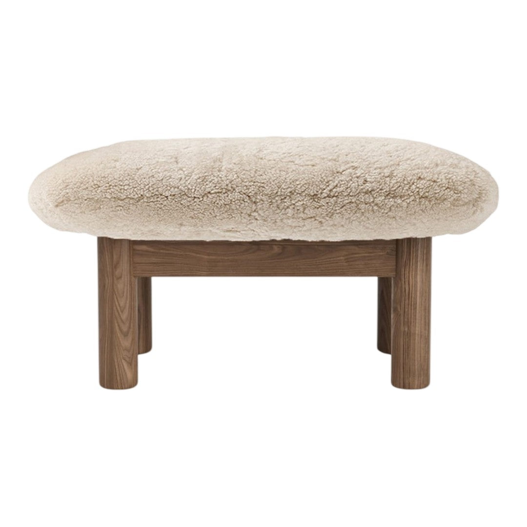 Beige plush ottoman with a rounded top and natural wood legs, featuring a soft, textured surface. Perfect for cozy interiors.