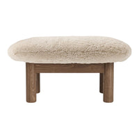 Beige plush ottoman with a rounded top and natural wood legs, featuring a soft, textured surface. Perfect for cozy interiors.