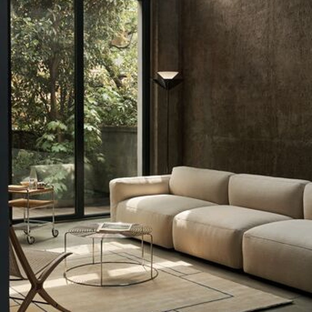 Neutral beige sofa paired with a minimalist glass table, set against an earthy textured wall and green outdoor view.