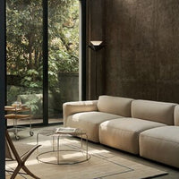 Neutral beige sofa paired with a minimalist glass table, set against an earthy textured wall and green outdoor view.