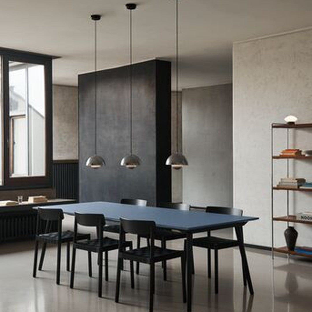 Modern dining room with a navy blue table, black chairs, and sleek metallic pendant lights against a neutral backdrop.