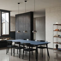 Modern dining room with a navy blue table, black chairs, and sleek metallic pendant lights against a neutral backdrop.