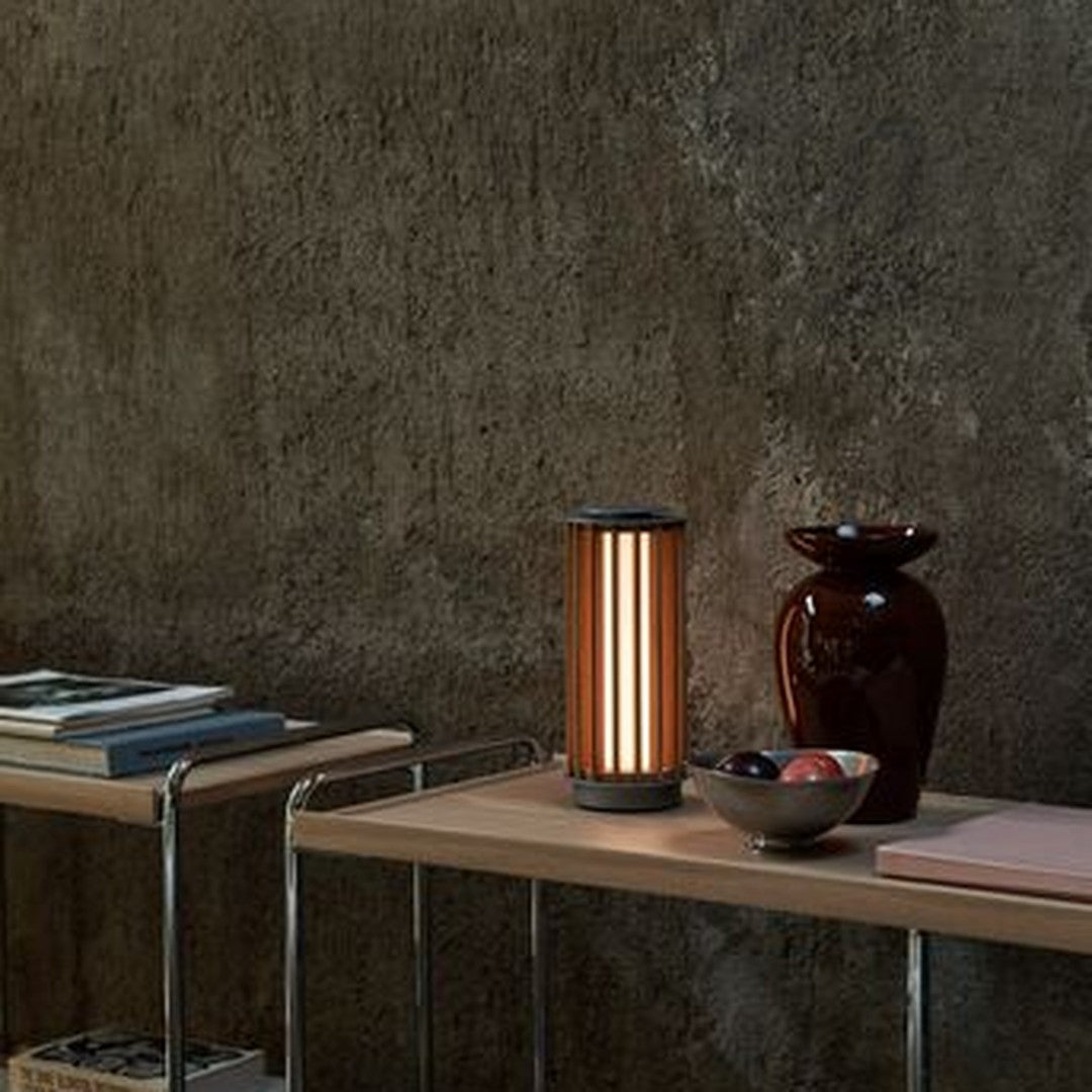 Modern lamp with vertical orange stripes, paired with glossy burgundy vase and ceramic bowl on log shelf.