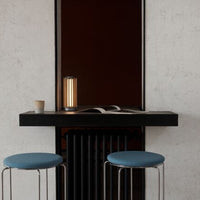 Blue padded stools with sleek chrome legs against a textured white wall and dark accent, featuring warm lighting.