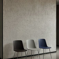 Three sleek chairs in dark brown, light gray, and navy blue against a textured gray wall background.