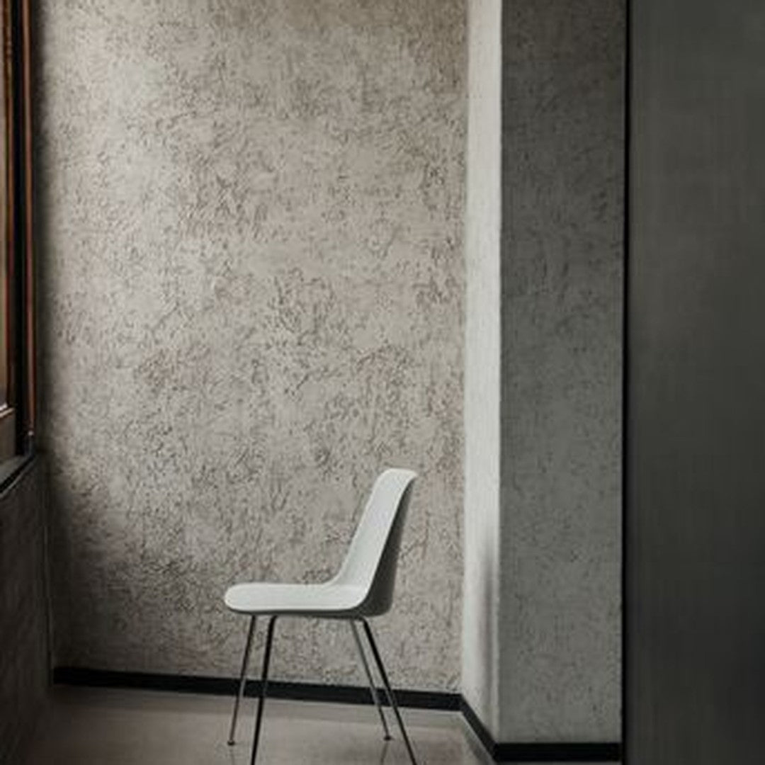 Minimalist white chair against a textured gray wall, highlighting modern design and subtle color contrasts.