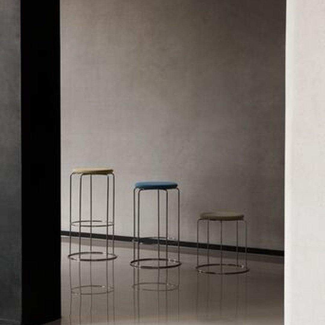 Three modern bar stools in muted tones of blue, green, and yellow against a sleek, minimalist backdrop.
