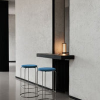 Blue upholstered bar stools against a minimalist gray backdrop with black accents and warm lighting.