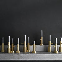 Brass and gray candle holders in an arranged display on a concrete surface against a dark background.