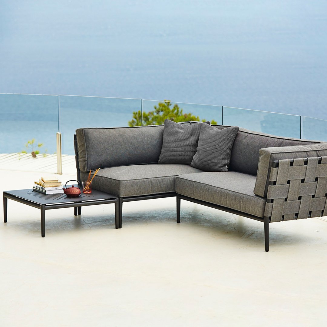 Gray sectional sofa with square-patterned woven backrest and matching cushions, complemented by a sleek black side table.