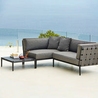 Gray sectional sofa with square-patterned woven backrest and matching cushions, complemented by a sleek black side table.