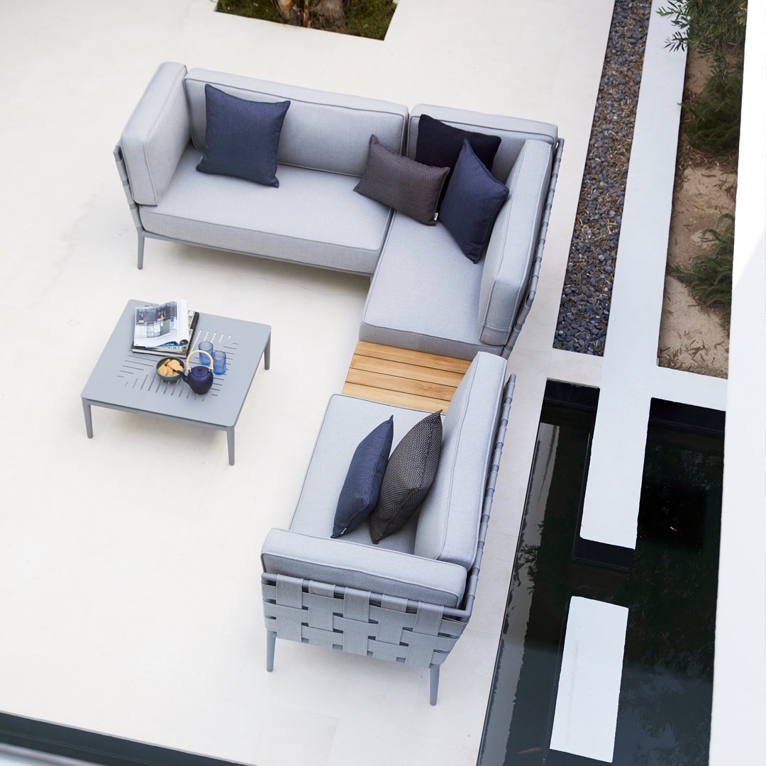 Modern L-shaped outdoor sofa in light gray with dark blue and purple accent pillows, paired with a sleek gray coffee table.