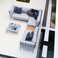 Modern L-shaped outdoor sofa in light gray with dark blue and purple accent pillows, paired with a sleek gray coffee table.