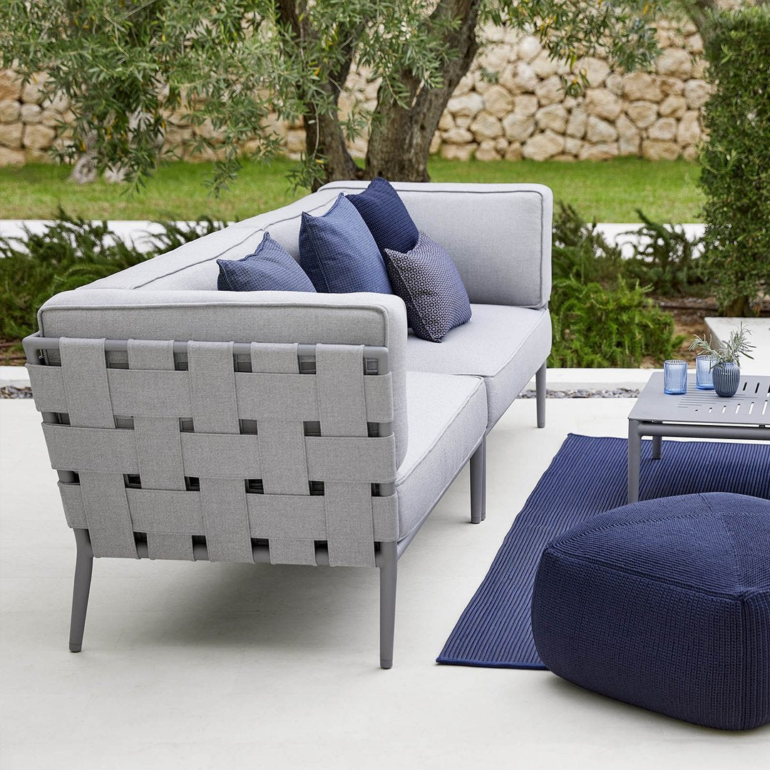 Gray wicker outdoor sofa with dark blue accent pillows, featuring a modern design in a tranquil garden setting.