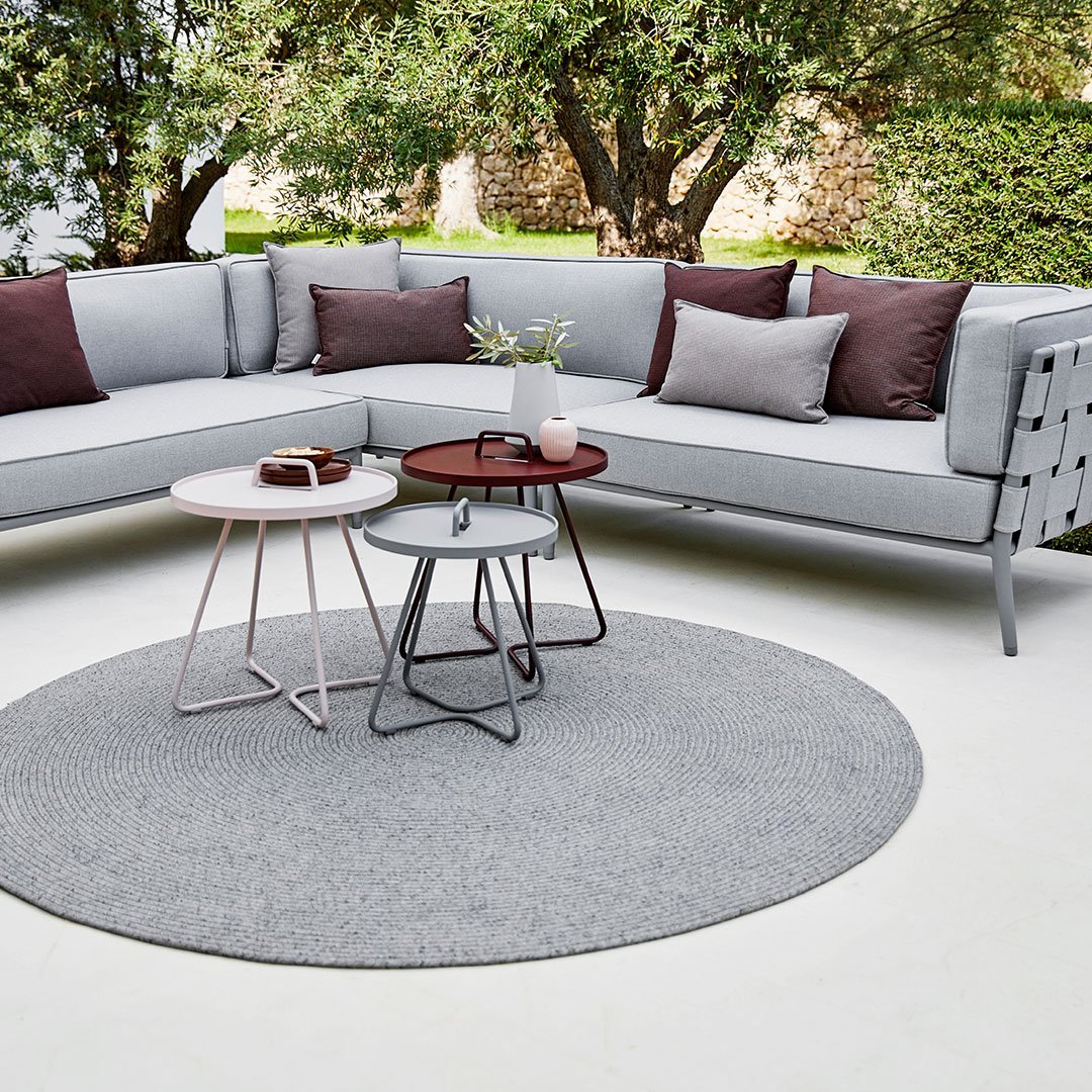 "Light gray sectional sofa with burgundy pillows and round gray rug, featuring modern metal tables in white and brown."