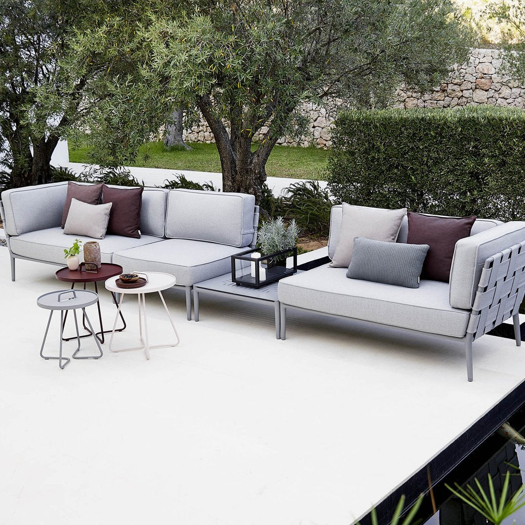 Stylish gray outdoor sectional sofa with solid and patterned cushions in earth tones, set against lush greenery.