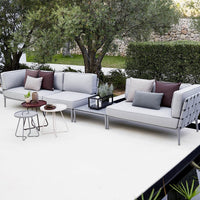 Stylish gray outdoor sectional sofa with solid and patterned cushions in earth tones, set against lush greenery.