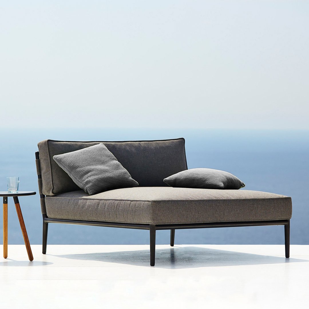 Stylish gray outdoor chaise lounge with two matching cushions, set against a serene blue ocean backdrop.