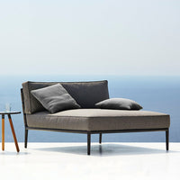 Stylish gray outdoor chaise lounge with two matching cushions, set against a serene blue ocean backdrop.
