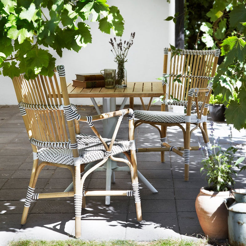 "Natural bamboo chairs with black and white striped cushions, set against a lush green backdrop."