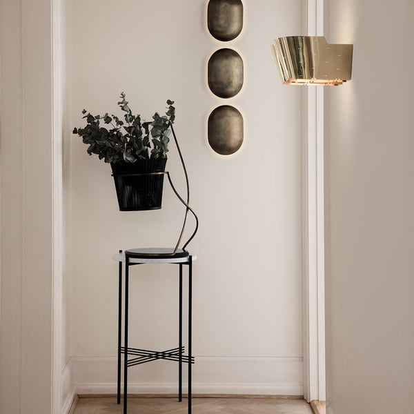 "Black plant stand with modern design, surrounded by gold wall decor and green foliage for a stylish accent."