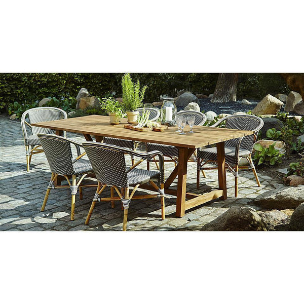 Natural wood table with gray woven chairs, featuring a rustic outdoor setting and green plant accents.