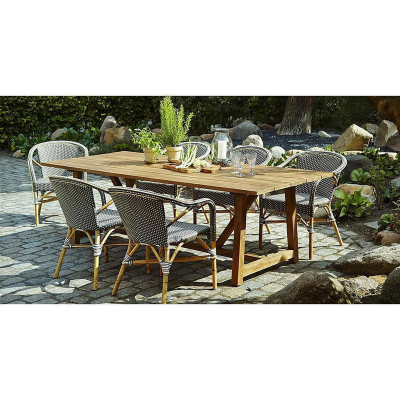 Natural wood table with gray woven chairs, featuring a rustic outdoor setting and green plant accents.