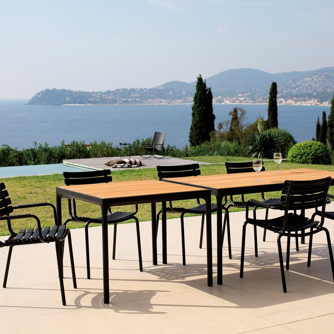 "Elegant black metal outdoor dining set with sleek lines and a warm wooden tabletop in a sunny coastal setting."