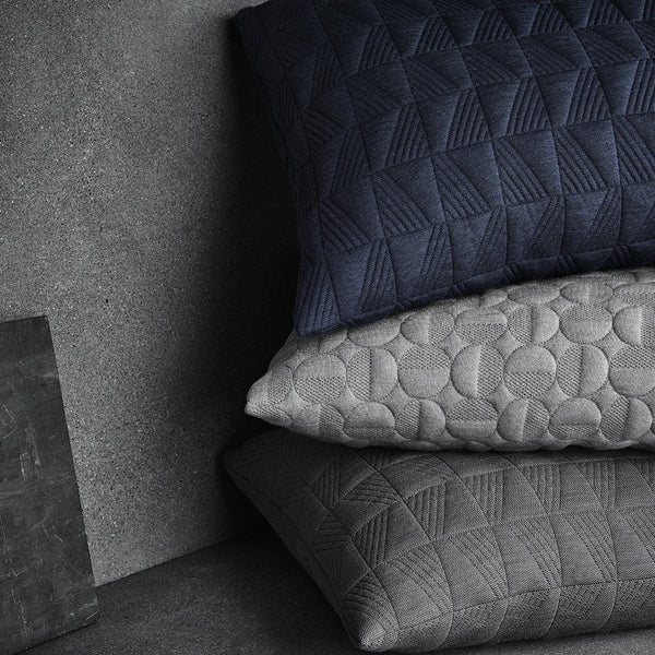 Textured pillows in navy, light gray, and dark gray, featuring geometric and circular patterns on a muted background.