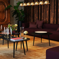 Luxurious burgundy sofa with gold accents, paired with a sleek black coffee table on a warm beige rug, featuring elegant decor.