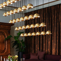 Modern chandelier with gold dome shades, suspended in front of rich brown textured curtains and deep purple furnishings.