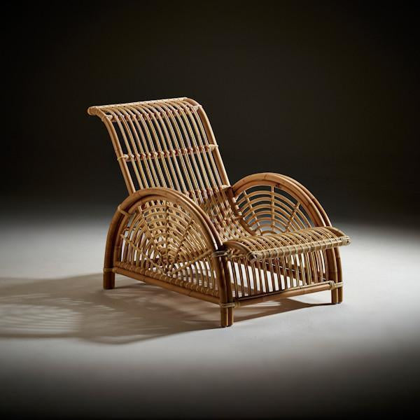 Natural rattan lounge chair in a light brown hue with a woven, curved design and open slat patterns.