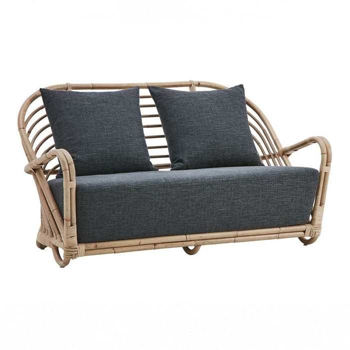Stylish rattan sofa in natural tones with grey cushions and striped accent pillows for modern decor.