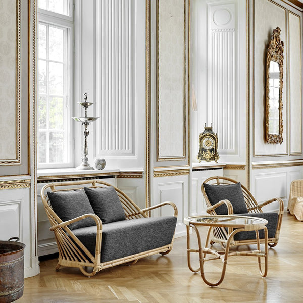 Gray upholstered sofa with rattan frame and light wooden accents in an elegant, light-filled room.