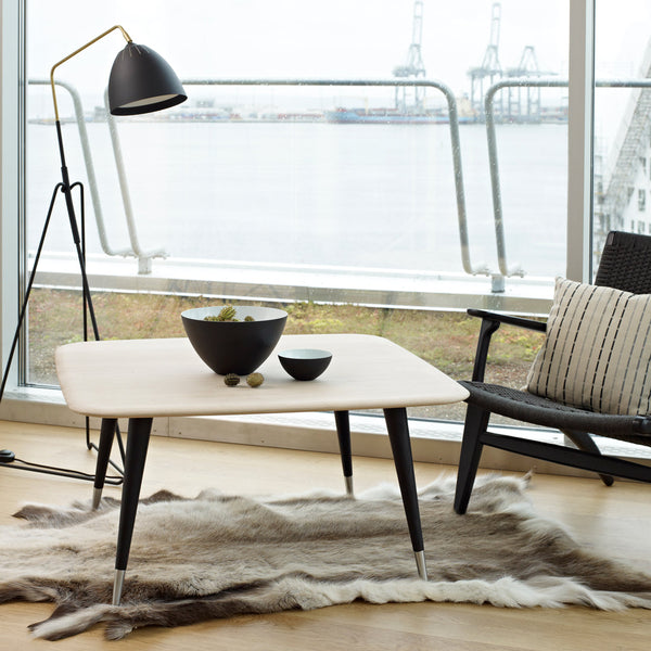 "Modern light-colored coffee table with sleek black legs and a minimalist design, paired with a plush fur rug."
