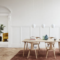 Light wood table with white chairs on a warm brown rug; bright white walls and green accents create a modern, airy atmosphere.