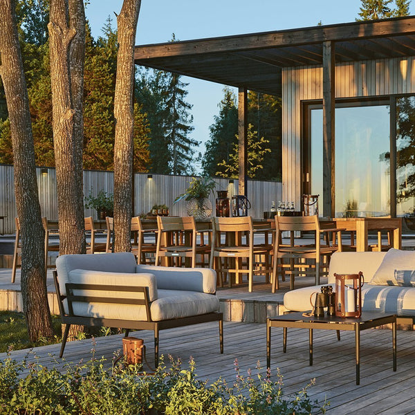Modern outdoor furniture set featuring neutral-colored cushions and natural wood tones against a backdrop of greenery.