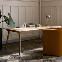 Wooden desk with a light finish, yellow armchair, and geometric patterned floor tiles in neutral tones.