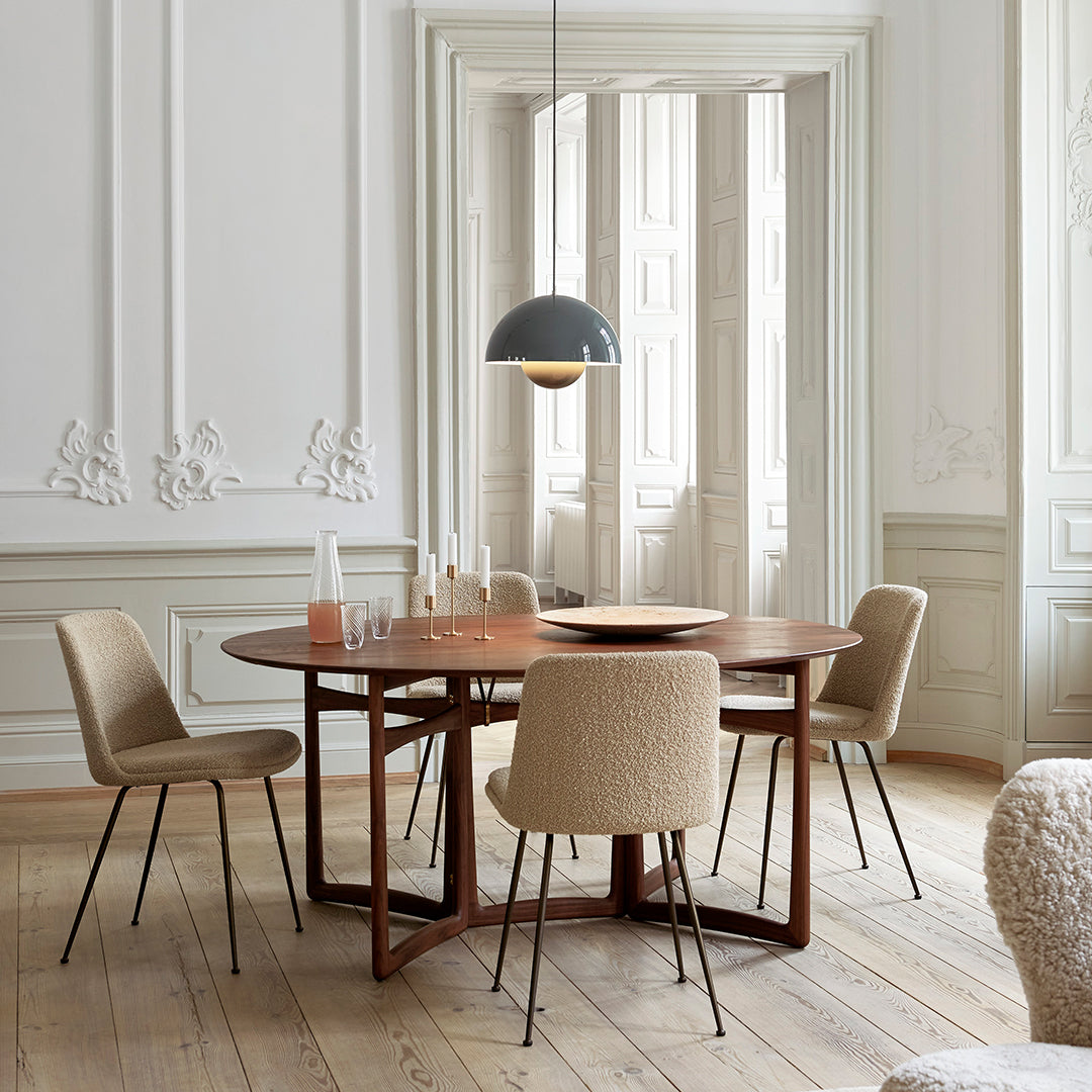 Round wooden dining table with warm brown tones, complemented by beige upholstered chairs and elegant white interior.