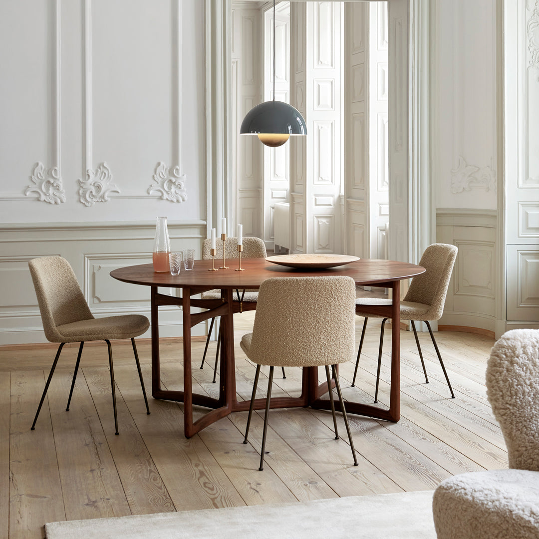 Modern round wooden dining table with beige textured chairs, complemented by a sleek black pendant light.