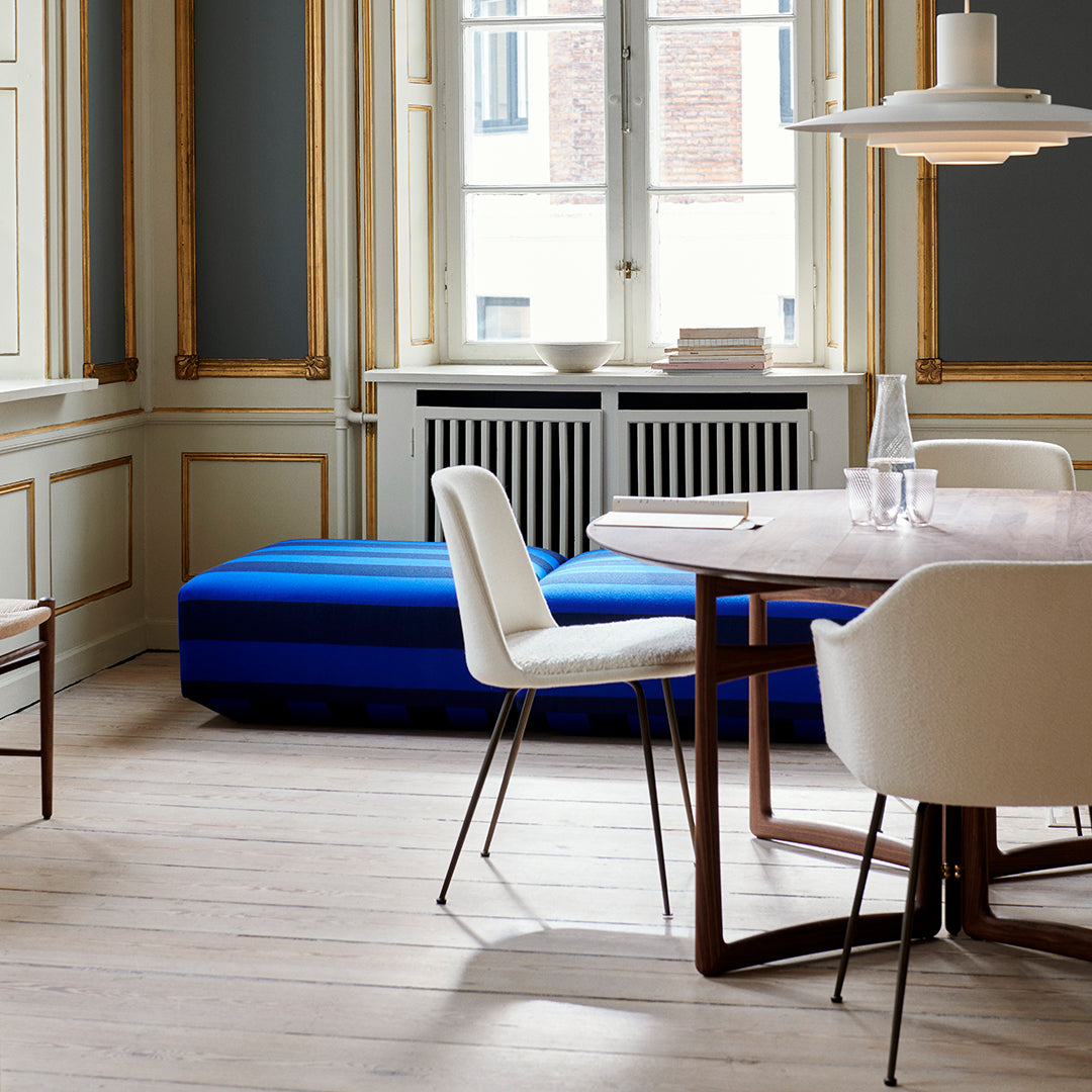 Modern blue lounge cushion with sleek lines, set against a neutral-toned room with wooden floors and white chairs.