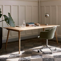 Light wood desk with green chair, surrounded by a black planter and patterned gray floor tiles.