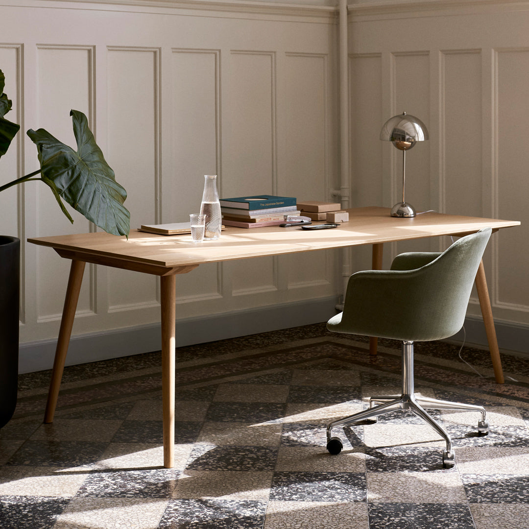 Light wood desk with green chair, surrounded by a black planter and patterned gray floor tiles.