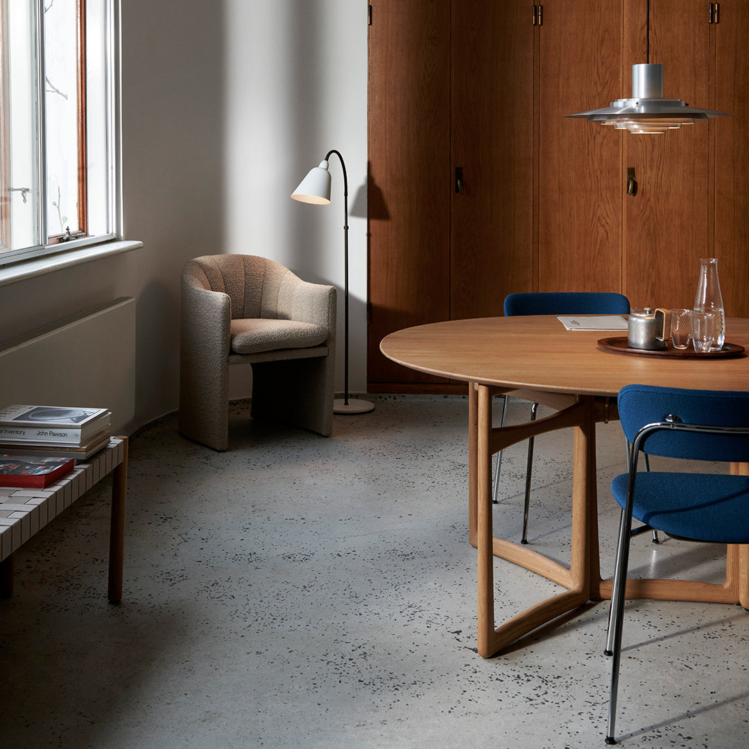 Modern dining space featuring a round wooden table, blue chairs, and warm wood textures, with a gray concrete floor.