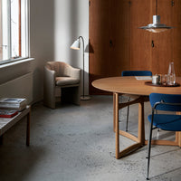 Modern dining space featuring a round wooden table, blue chairs, and warm wood textures, with a gray concrete floor.