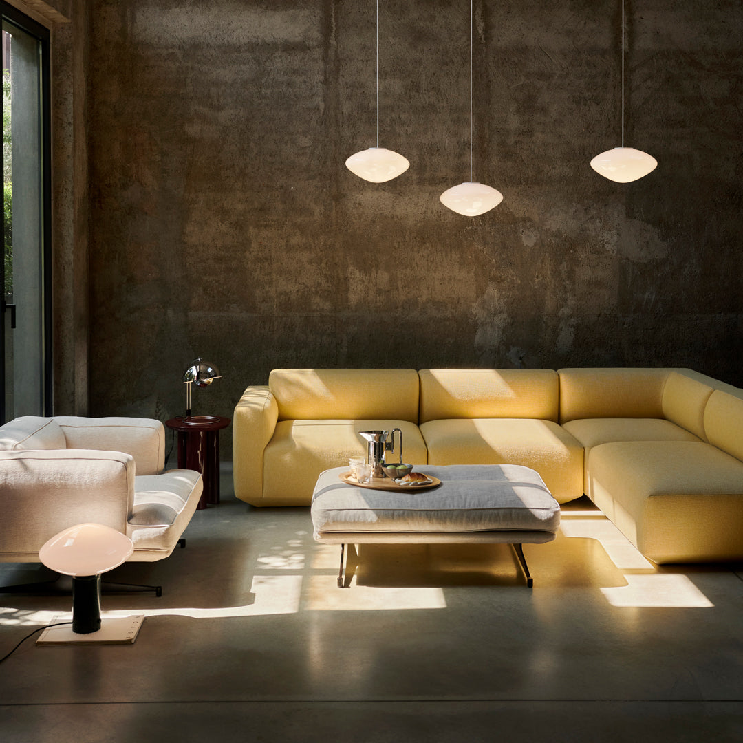 Modern living room featuring a yellow sectional sofa, white armchair, and minimalist decor against a textured gray wall.