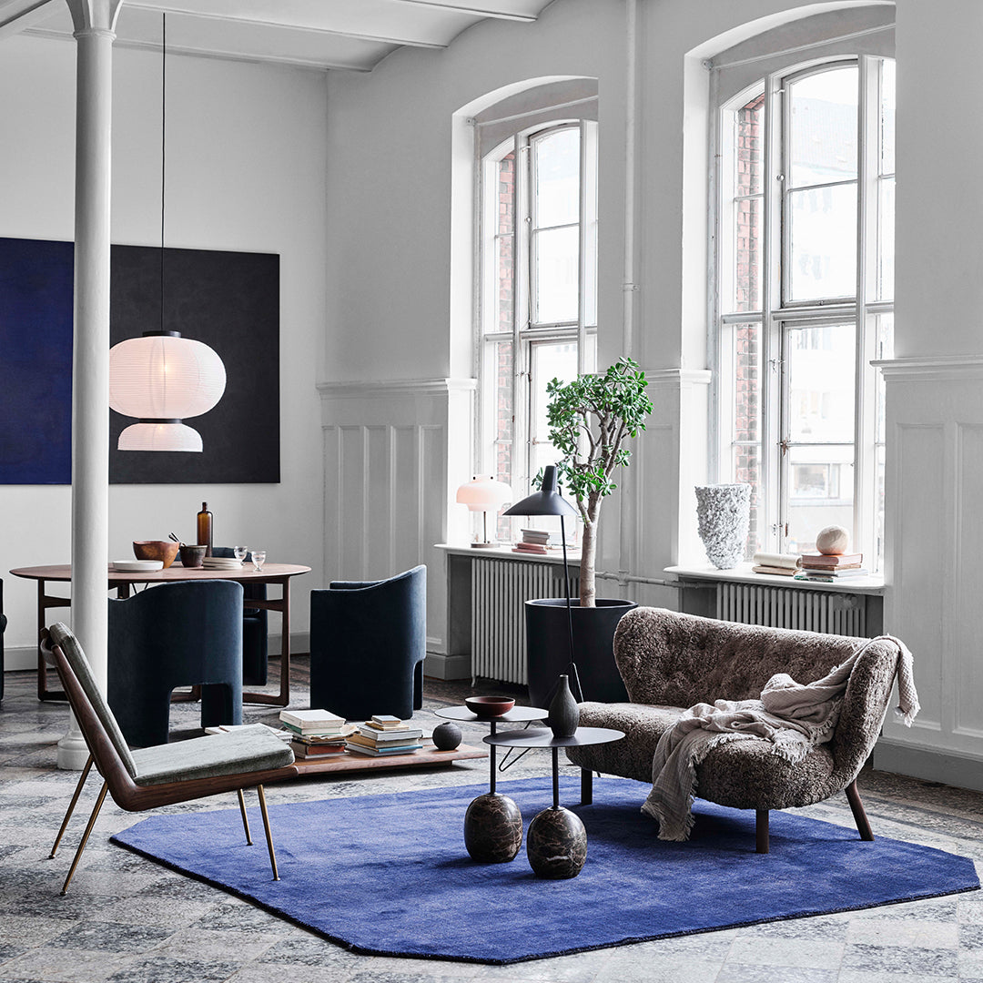 Modern living room featuring a blue rug, gray and white walls, and dark green accent chairs with a neutral patterned sofa.