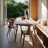 Modern wooden dining table with natural finish, accompanied by light wood chairs, set in a bright, green-accented space.