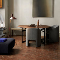 Round wooden dining table with gray upholstered chairs, featuring earthy tones and a textured floor pattern.